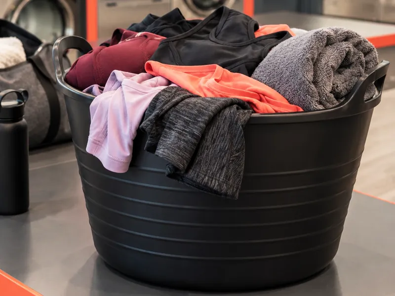 Cesto pieno di abbigliamento sportivo e un asciugamano, con borsa e borraccia sul bancone della lavanderia